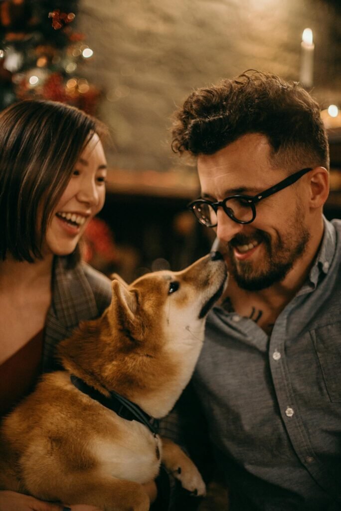 Smiling couple sharing a joyful moment with their Shiba Inu dog indoors.