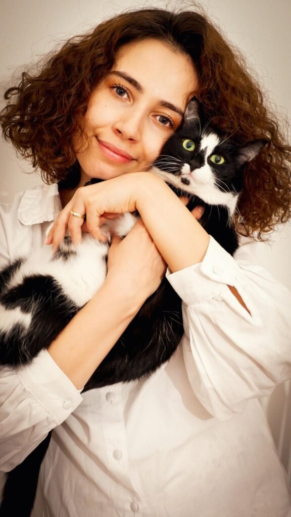 Woman with curly hair holding her black and white cat in a warm embrace, smiling.